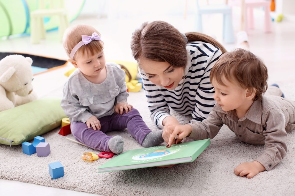 Teacher reading to two children on floor.